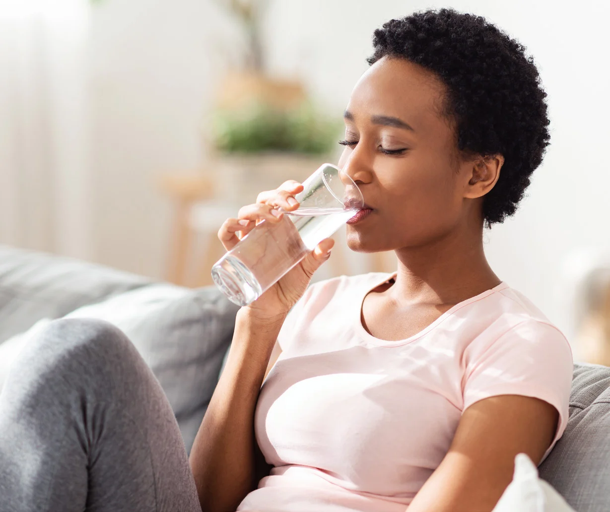 A woman drinks a glass of water at home