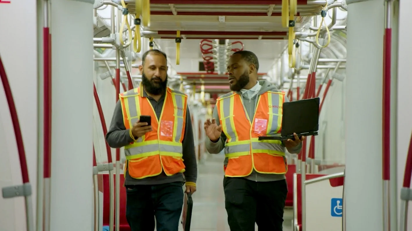 Two workers in high-visibility vests check devices on a TTC train