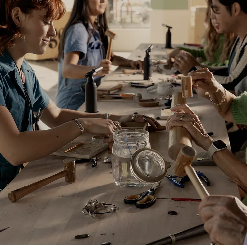 Women make jewellery at a shared workshop table