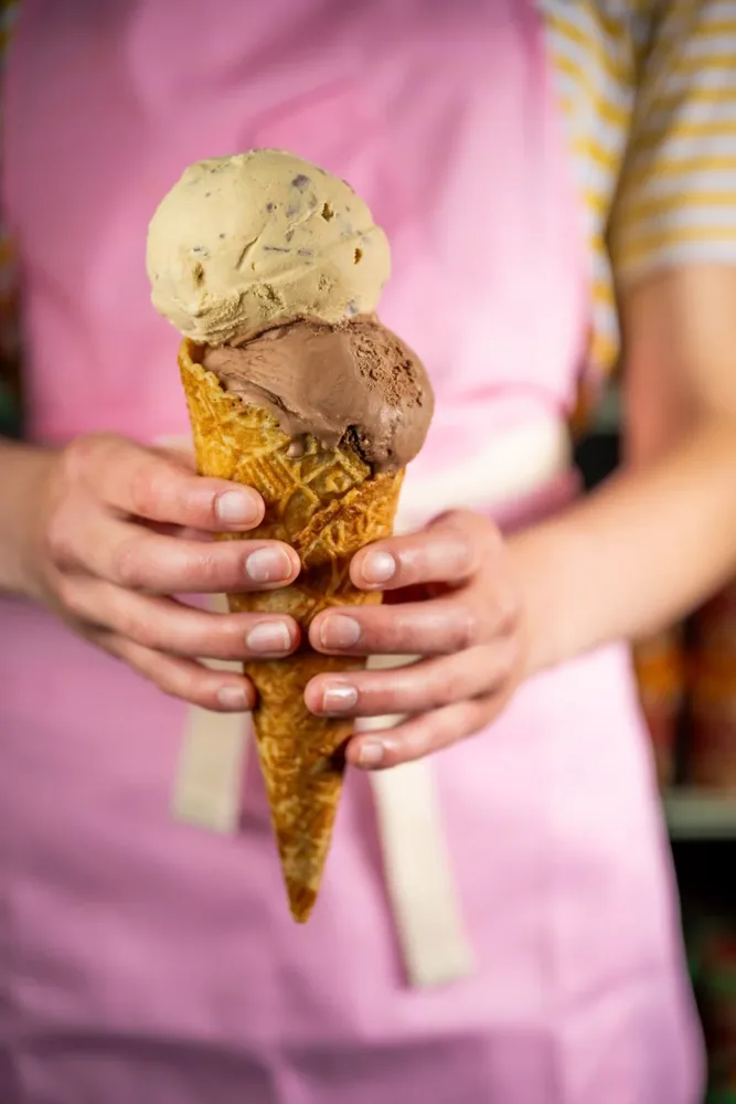 A person holds a waffle cone with three scoops of ice cream