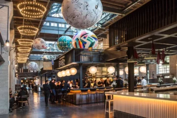 Warmly lit stalls and globe sculptures under Waterworks Food Hall’s tall ceiling