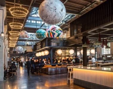 Warmly lit stalls and globe sculptures under Waterworks Food Hall’s tall ceiling