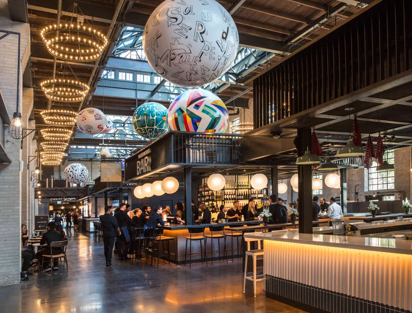 Warmly lit stalls and globe sculptures under Waterworks Food Hall’s tall ceiling