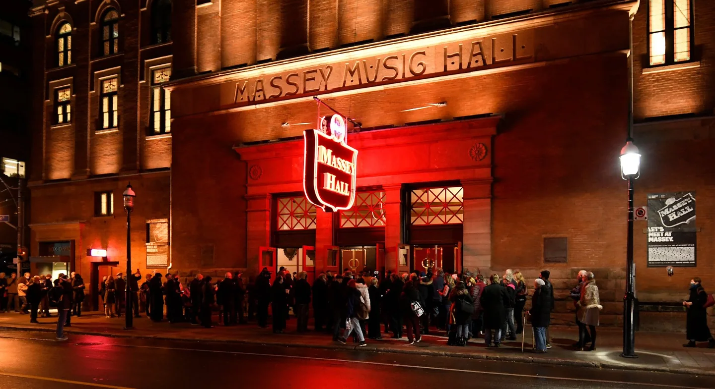 Concertgoers outside Massey Hall under its red neon sign