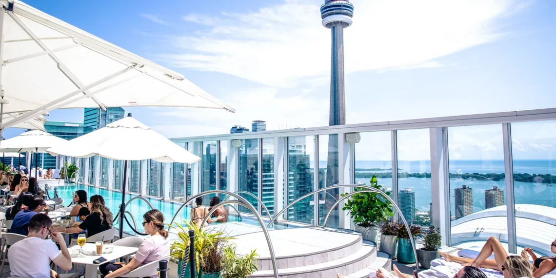 Guests relax beside Bisha Hotel Toronto's rooftop pool with the CN Tower, Rogers Centre and Lake Ontario beyond