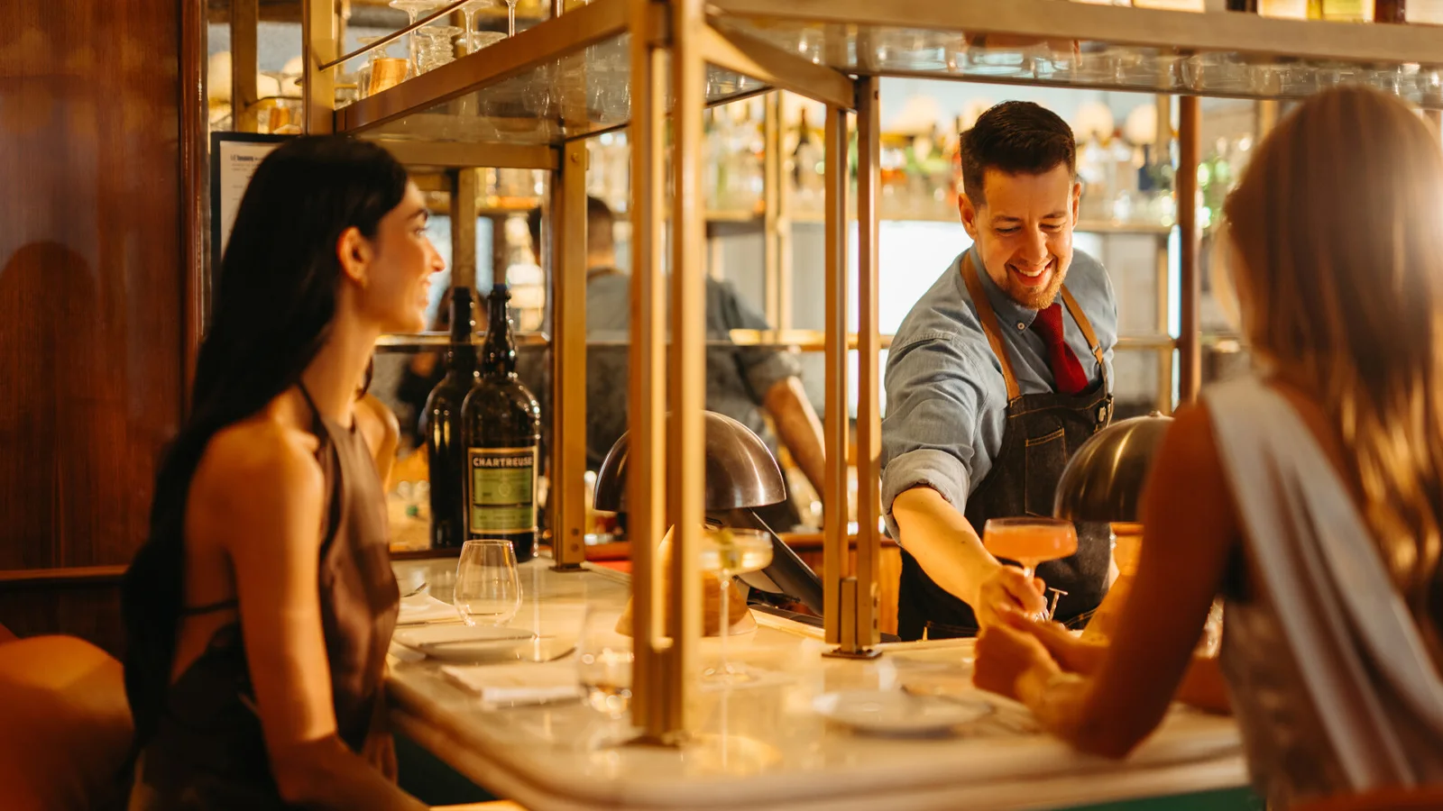 Two women sit at the bar while a bartender pours a drink at Four Seasons Hotel Toronto