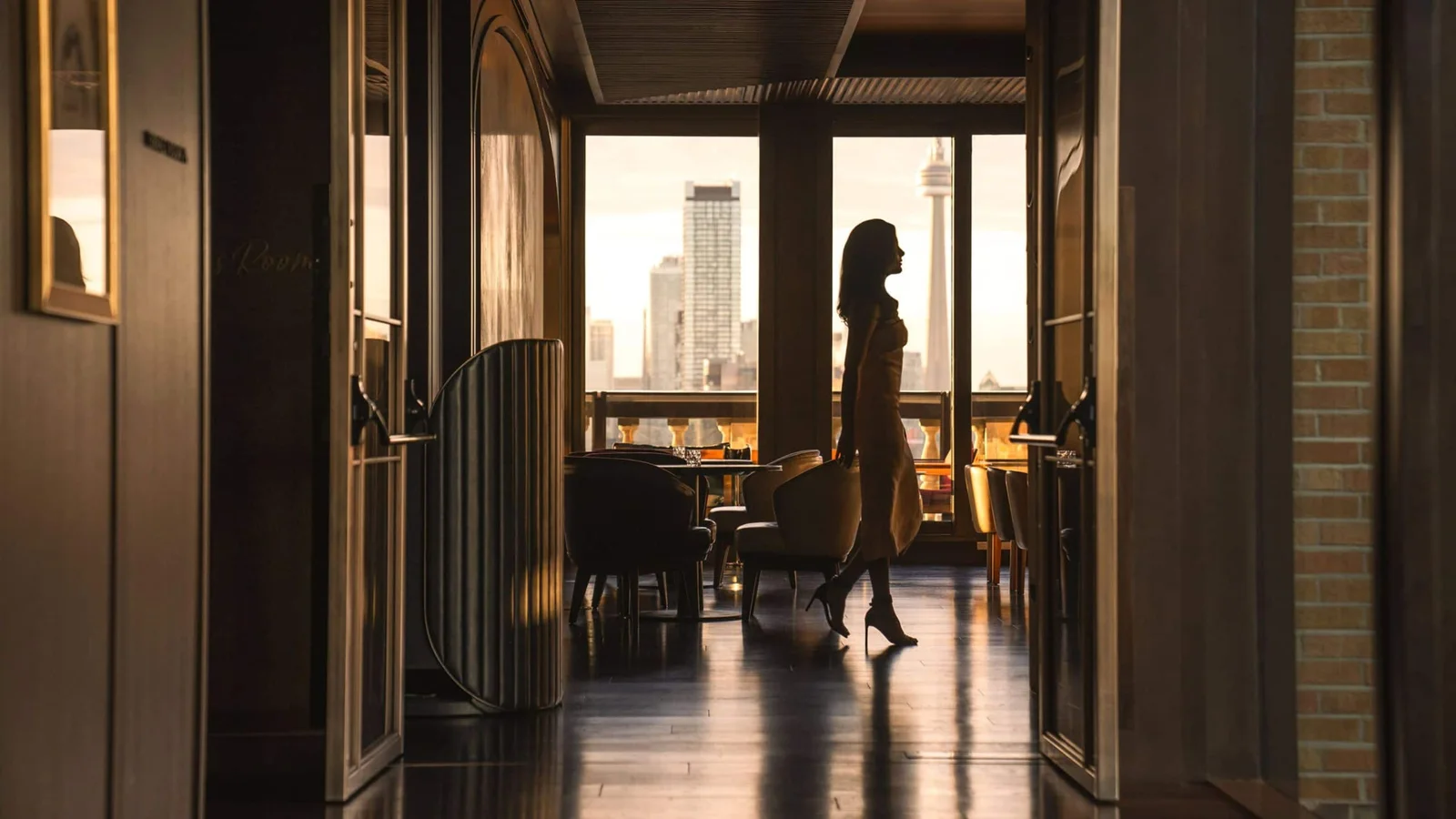 A woman enters Writers Room Bar with Toronto buildings visible through the windows