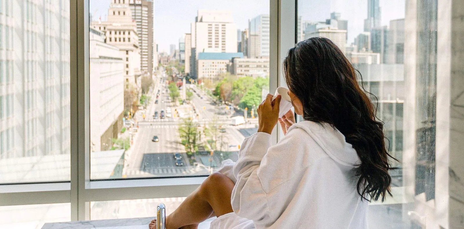 A woman in a robe sits by a window overlooking University Avenue