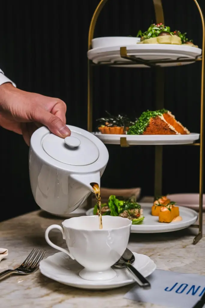 Tea poured into a cup beside a tiered stand of savouries and sweets at Joni