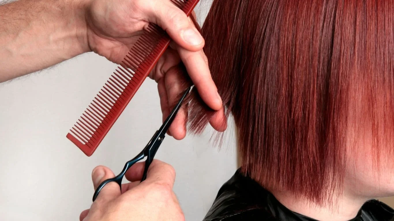 A stylist cutting a short red bob in a Marca College photograph.