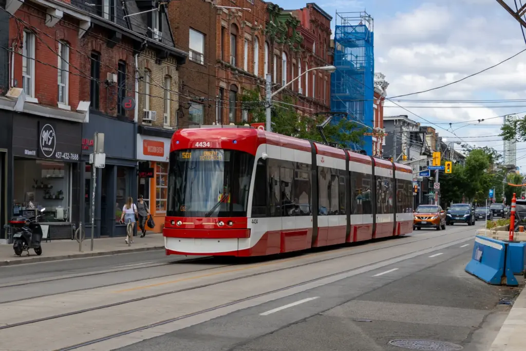 A modern 501 TTC streetcar sharing Queen Street West with traffic