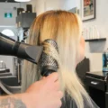 A stylist uses a round brush and dryer on blonde hair at Emerald.