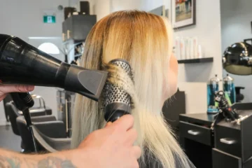 A stylist uses a round brush and dryer on blonde hair at Emerald.