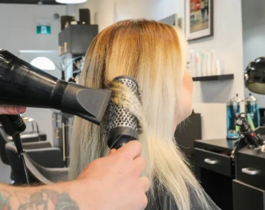 A stylist uses a round brush and dryer on blonde hair at Emerald.
