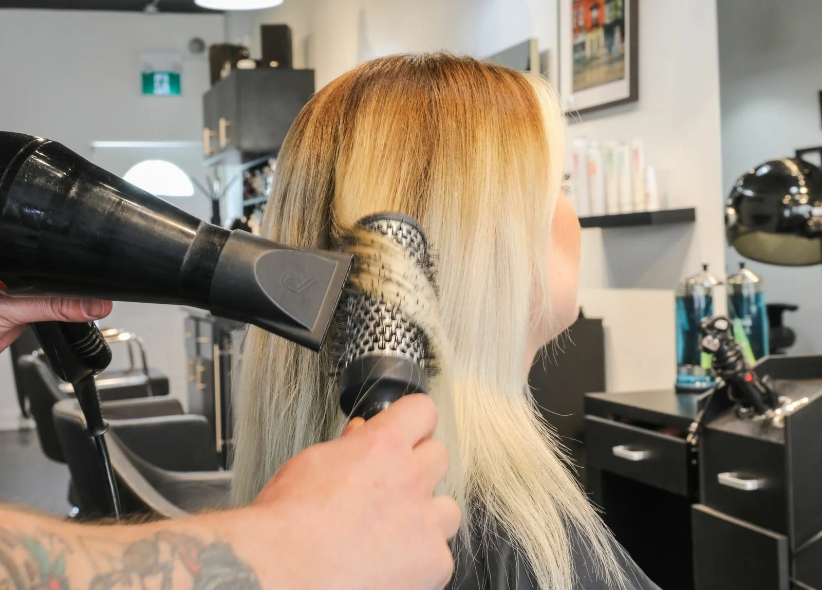 A stylist uses a round brush and dryer on blonde hair at Emerald.