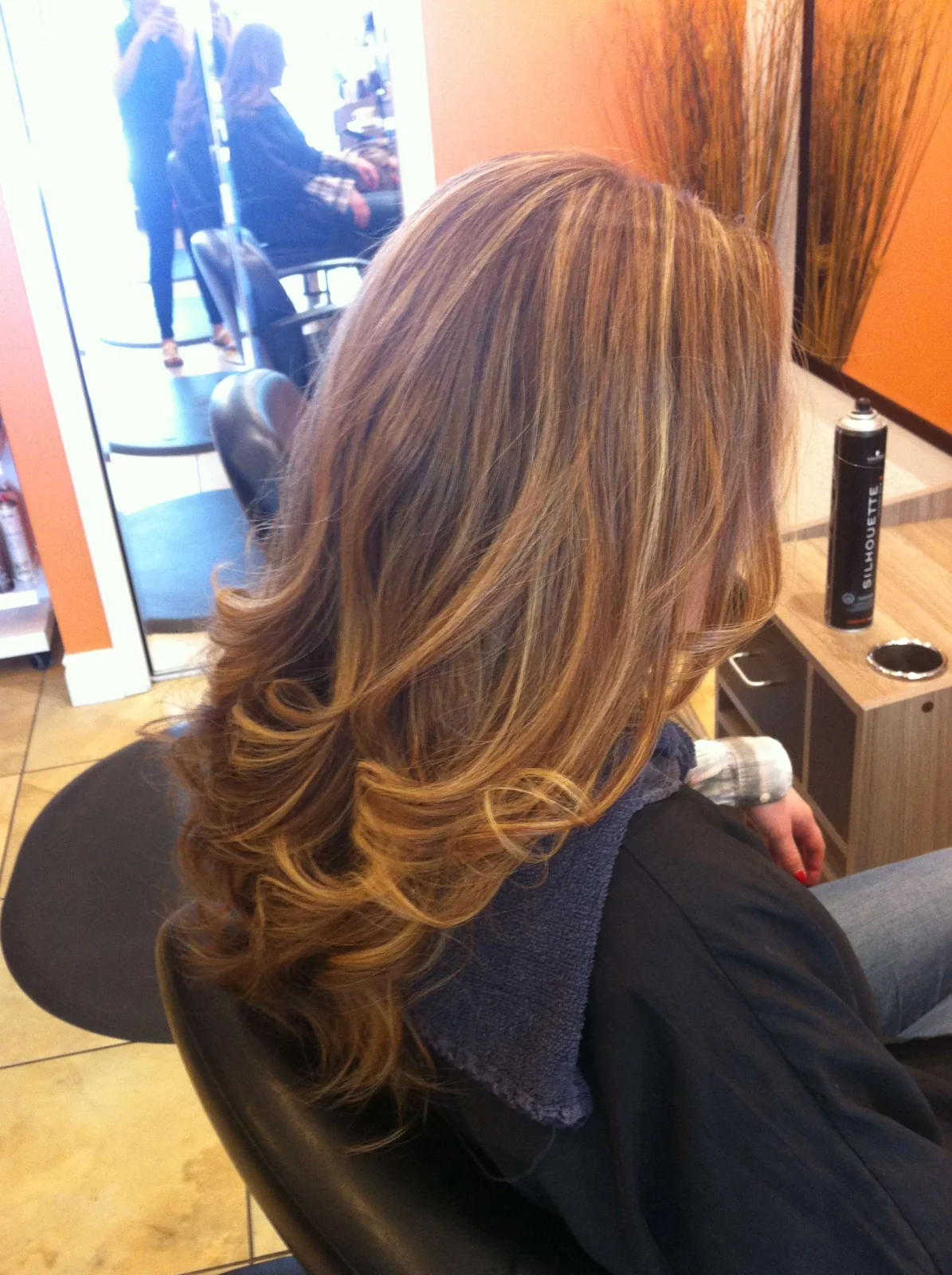 Warm brown hair with lighter sections, styled in loose waves.