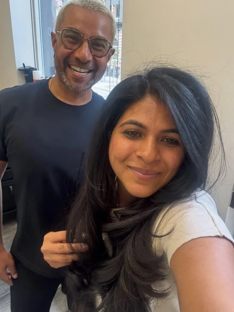 A smiling client with long, dark styled hair beside a stylist at H&CO.