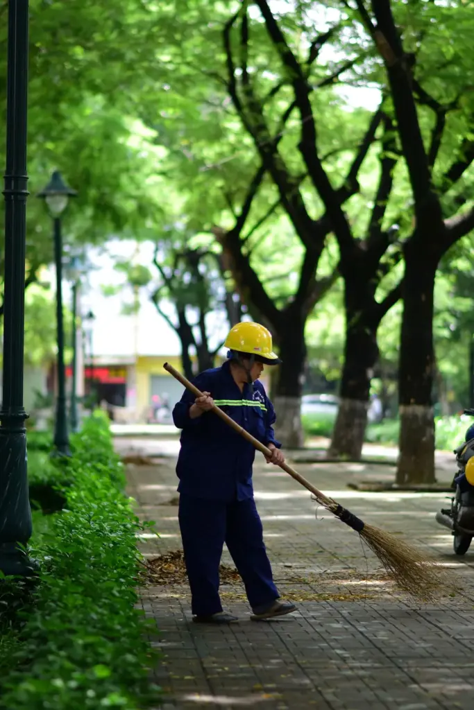 Maintenance worker sweeping a tree-lined public park path