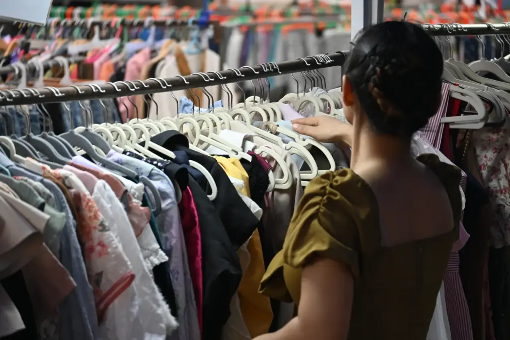 Woman browsing a tightly packed rack of colourful second-hand clothing