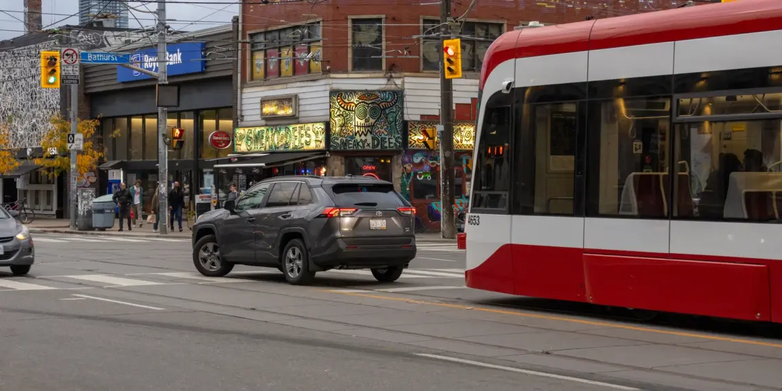 Modern TTC streetcar delayed behind a car making a left turn in Toronto
