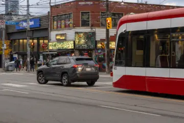 Modern TTC streetcar delayed behind a car making a left turn in Toronto