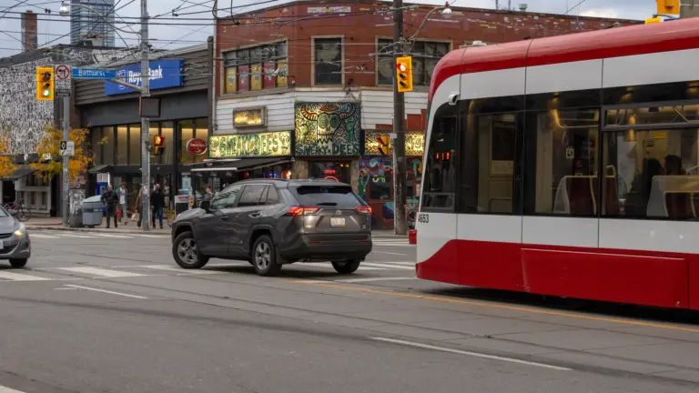 Modern TTC streetcar delayed behind a car making a left turn in Toronto