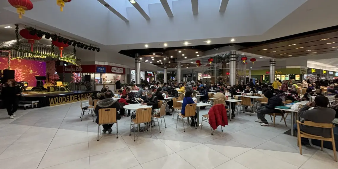 Crowded food court inside Woodside Square with red lanterns and many occupied tables