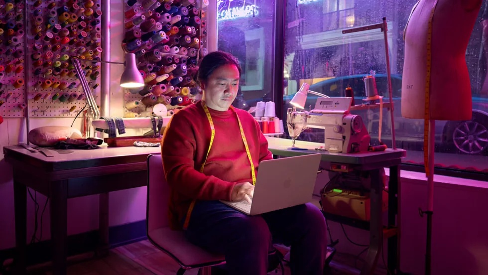 A person working on a MacBook Neo in a textile studio