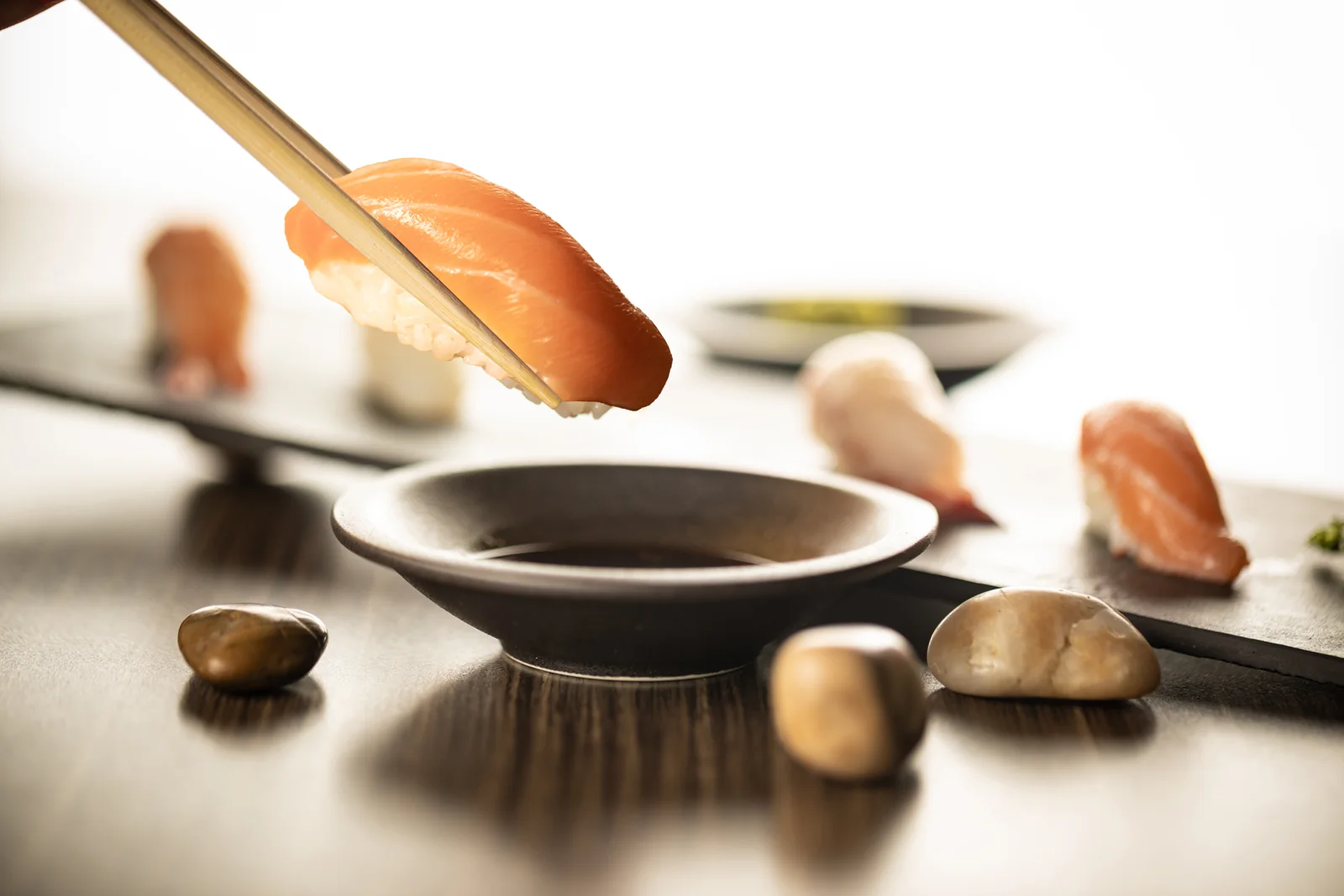 Chopsticks holding salmon nigiri above a soy sauce dish