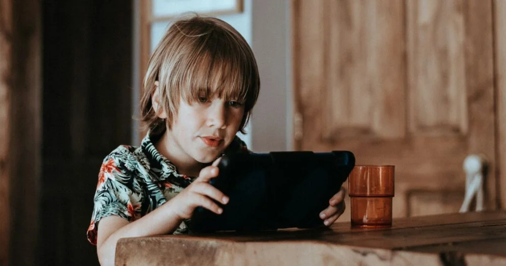 A child using a tablet at a wooden table.