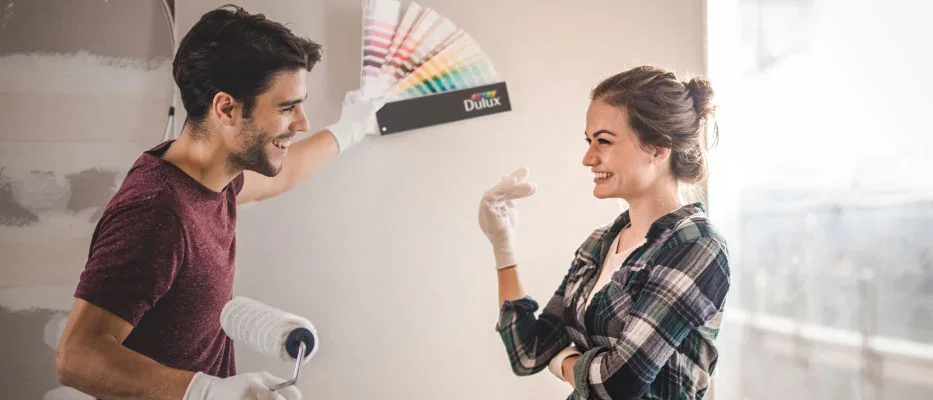 Two people comparing paint colours while painting a wall