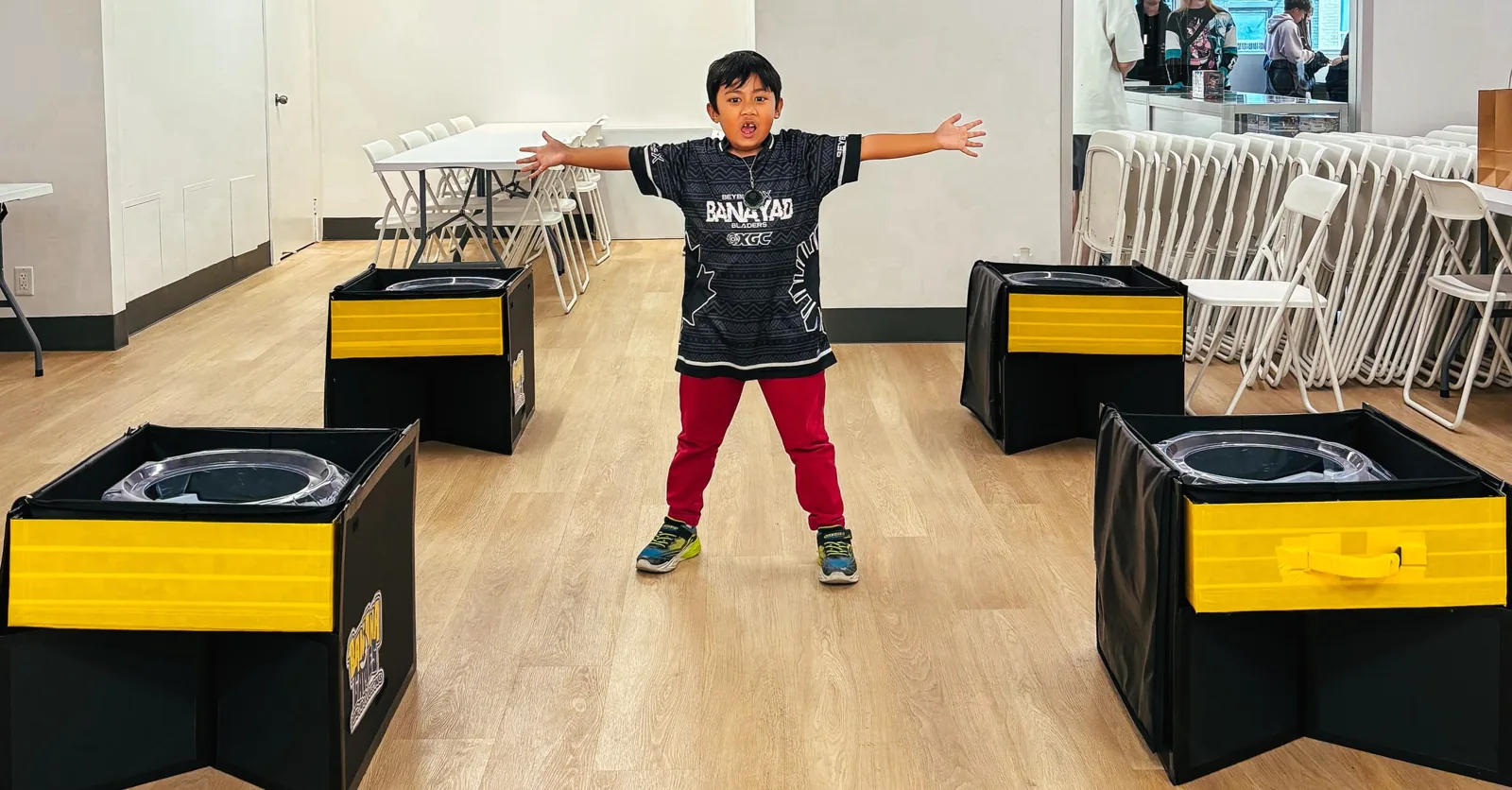 Young player standing between Beyblade stadiums set up at Banana Games