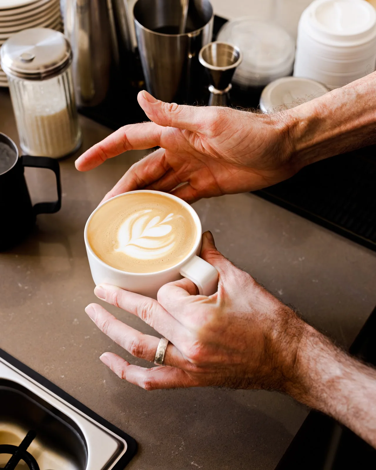 Hands presenting a cup of milk coffee at Alice Marie Bakery and Coffee