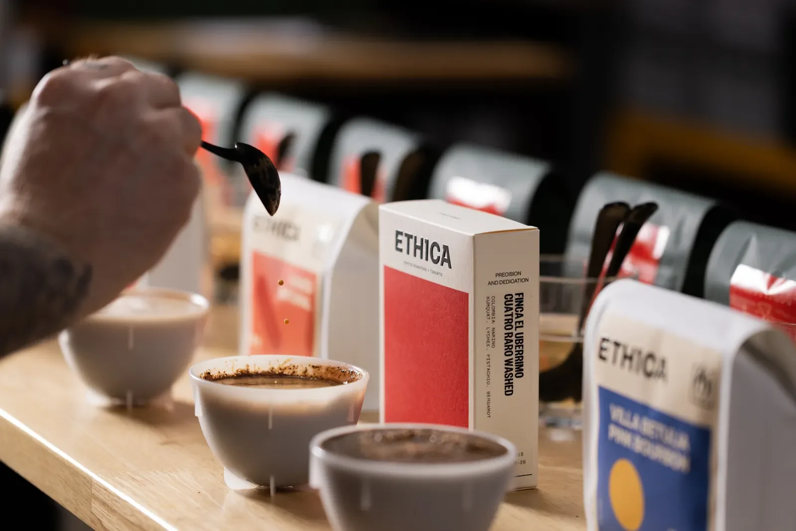 A person using a spoon to taste coffee from bowls at an Ethica cupping