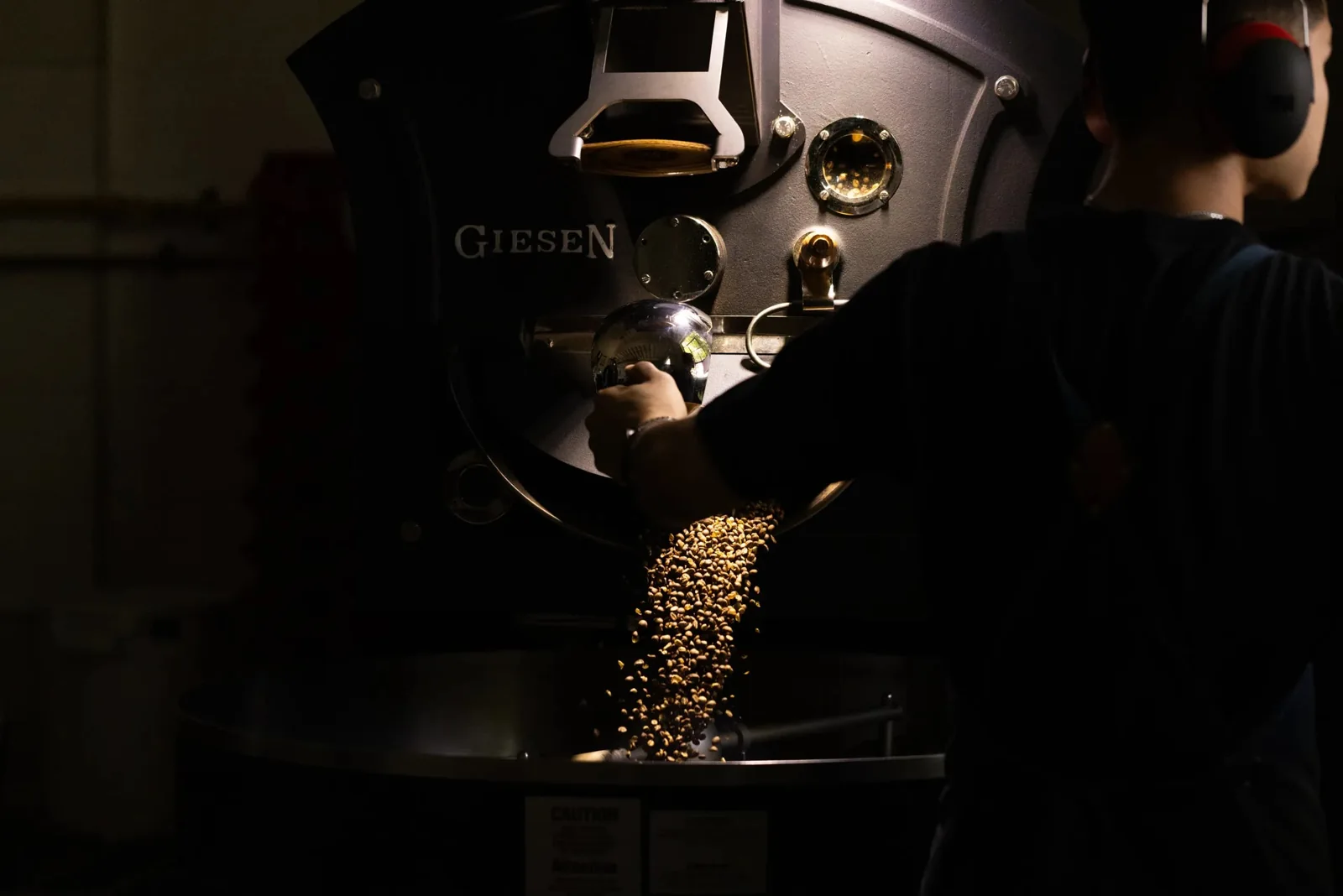 A worker at Ethica beside a roaster as roasted coffee beans are released
