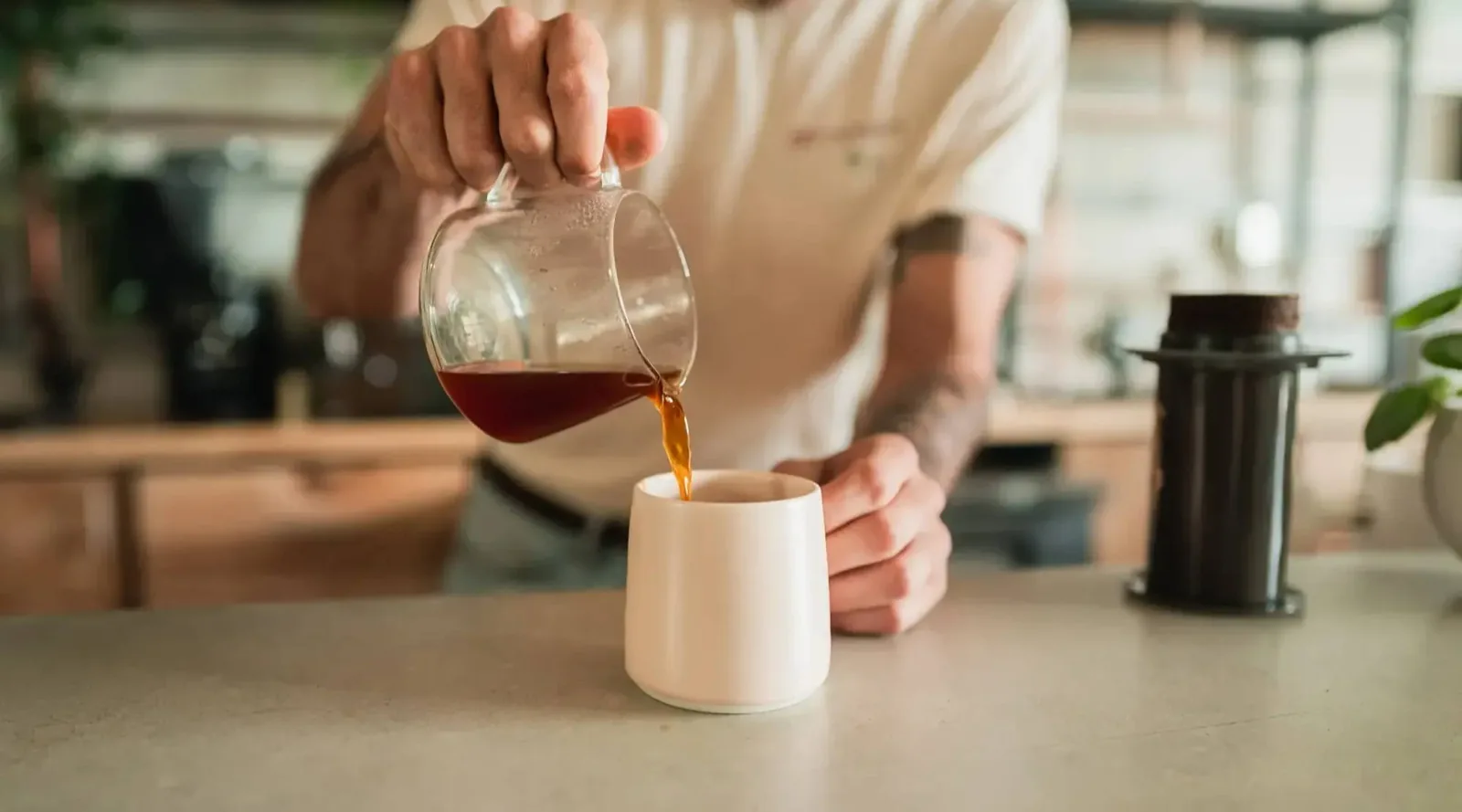 A person pouring filter coffee from a glass carafe into a white cup at Subtext
