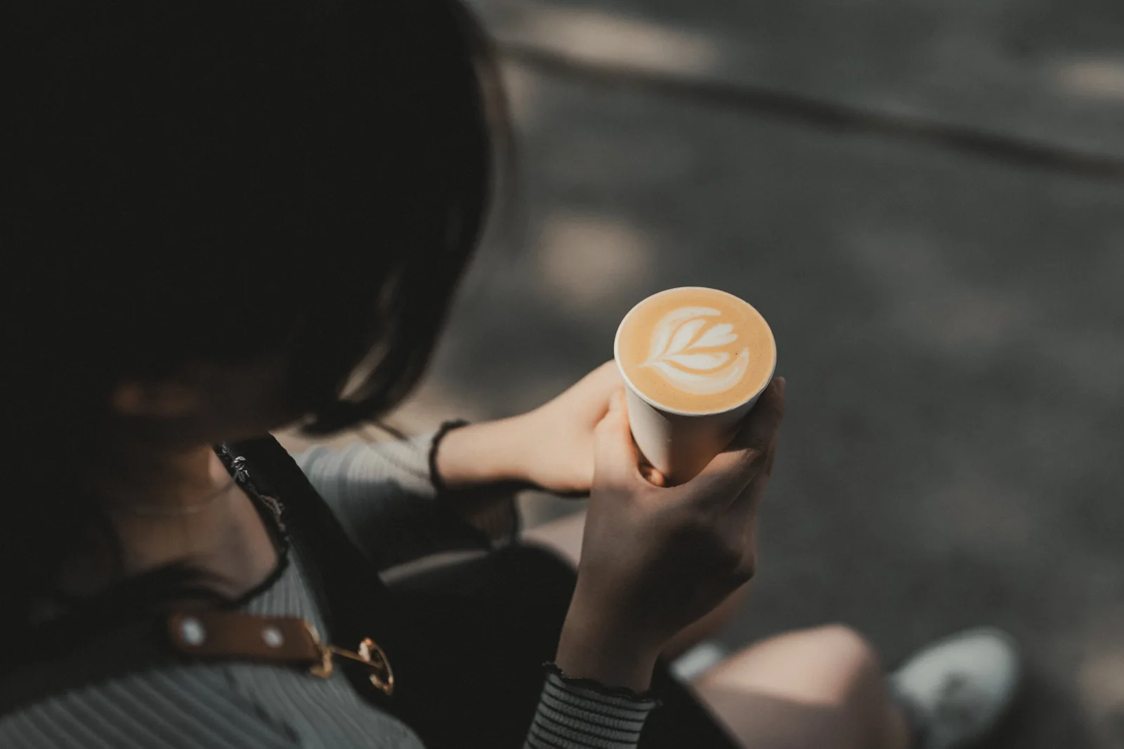 A person holding a paper cup of coffee with leaf-shaped latte art