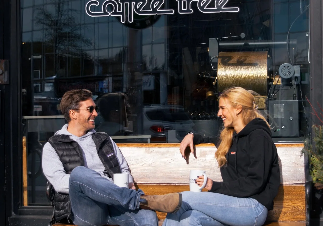 Two people sitting outside The Coffee Tree Roastery beside its front window