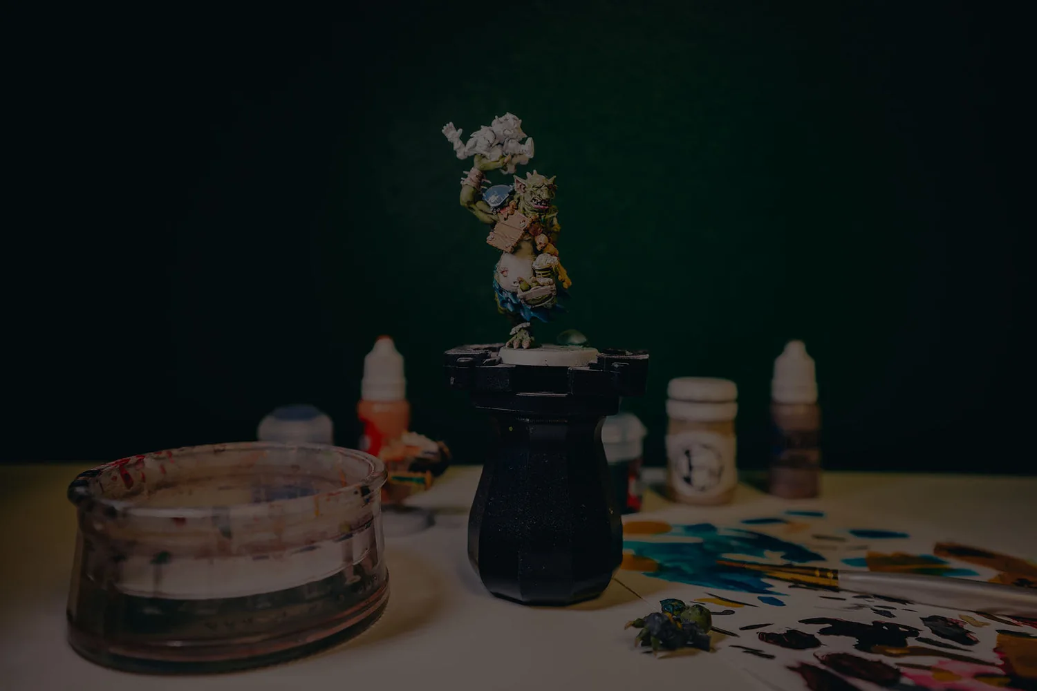A painted fantasy miniature beside brushes and paint pots