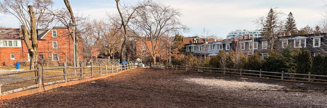 Wood-chip dog run and wooden fence at Baird Park with homes behind