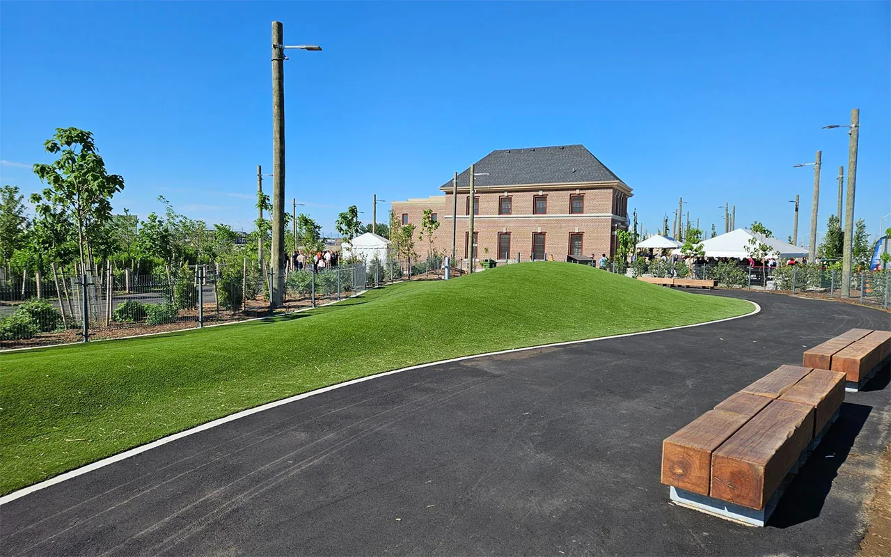 Curved turf and paved path within a fenced dog run beside Old Fire Hall 30