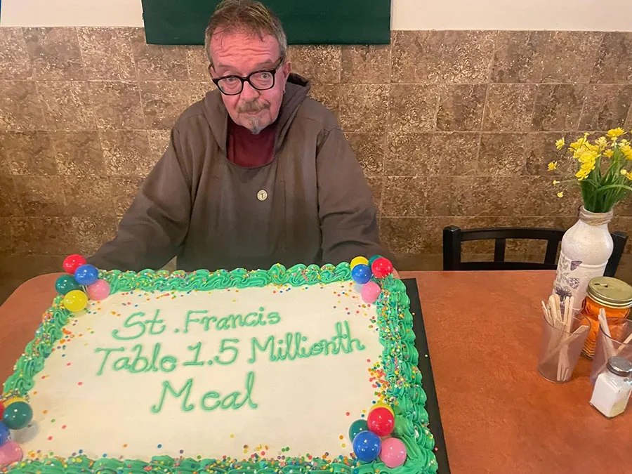 St. Francis Table friar seated behind a cake marking 1.5 million meals