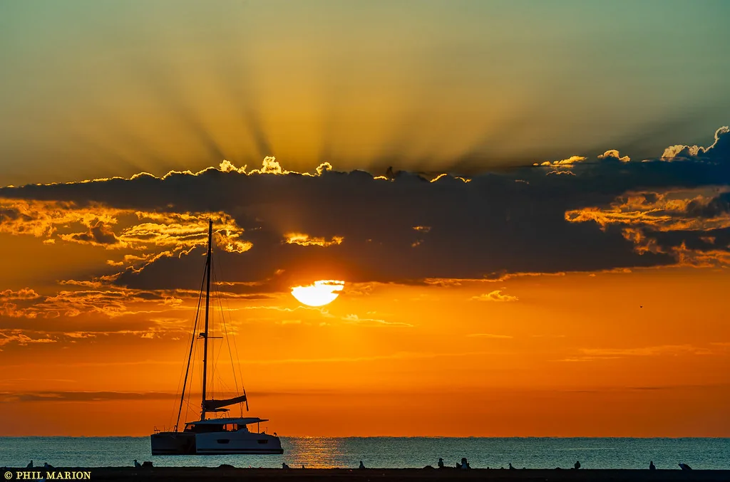 Golden sunrise behind clouds and a sailboat off Woodbine Beach