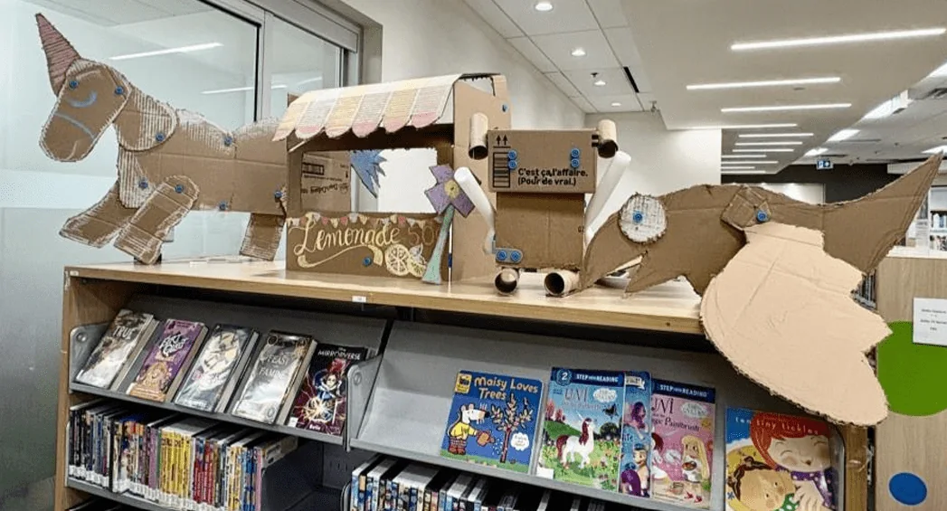 Cardboard horses and a wagon displayed above children’s books at a Toronto library