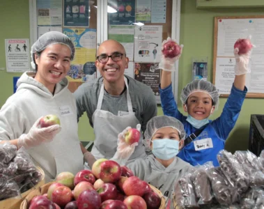 Smiling adults and children holding apples while volunteering at Good Shepherd’s Thanksgiving meal