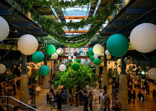 People at an event inside St. Lawrence Market North with hanging plants and balloons