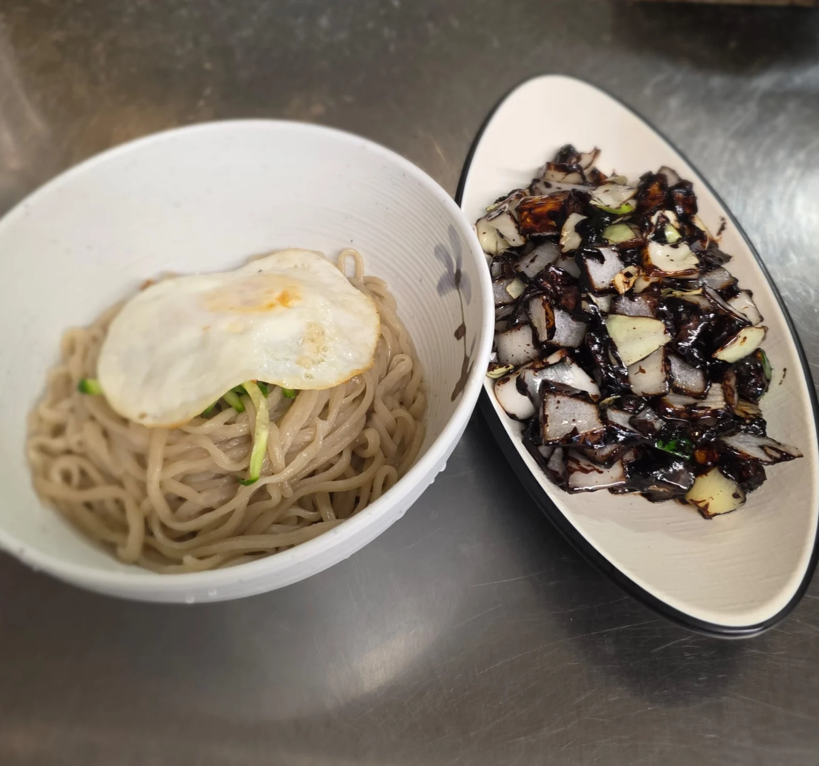 Noodles with an egg beside black-bean sauce and vegetables